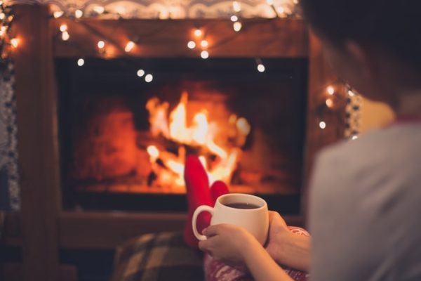 Woman sitting by fireplace enjoying cup of tea.
