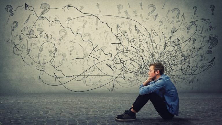 Young man sitting next to wall with erratic scribbles on it.