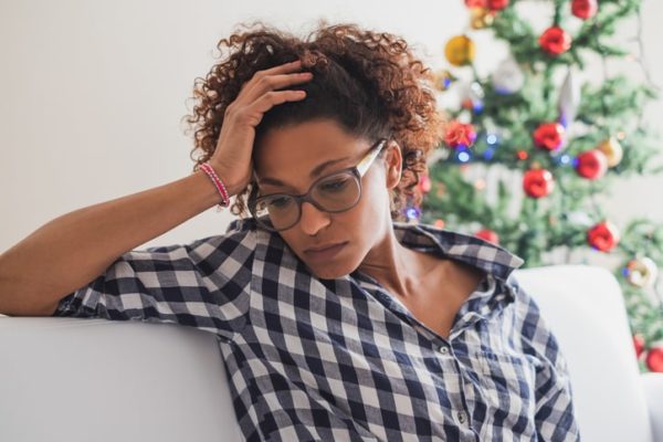 Stressed black woman sitting on couch next to Christmas tree.