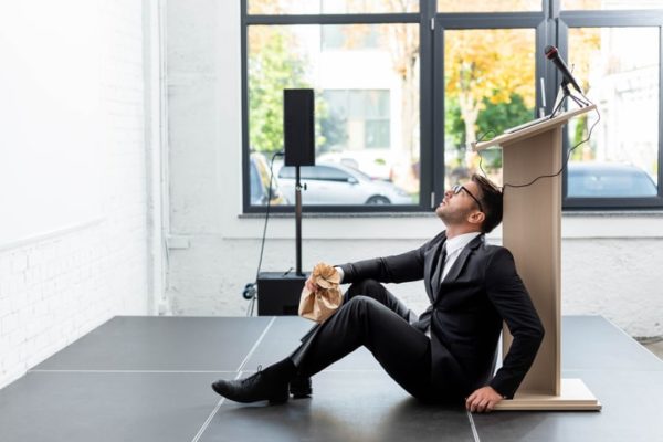 Side view of scared businessman in suit holding paper bag and sitting on floor during conference.