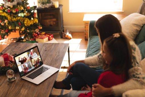Mother and daughter looking at laptop of loved ones on online call next to Christmas tree.