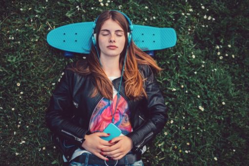 Teenage girl resting head on skateboard listening to music on headphones.