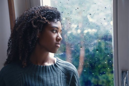 Isolated young girl looking out window as it rains outside.